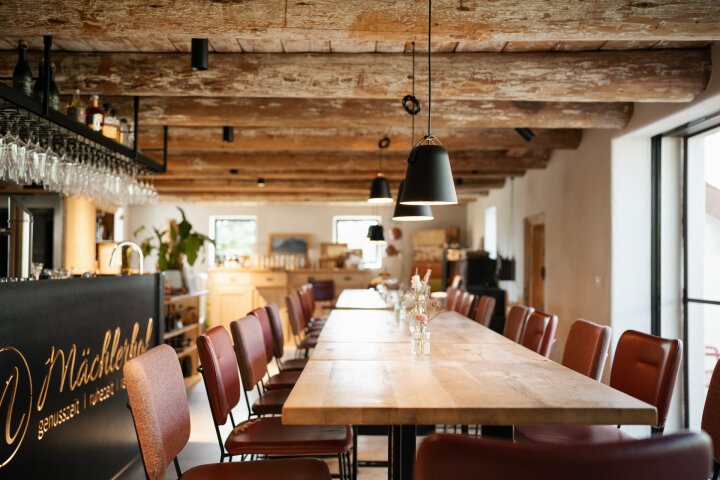 eine Innenansicht des Restaurants "Mächlerhof": ein langer Holztisch mit roten Leder-Stühlen ist zu sehen
